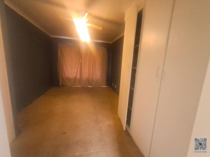 An empty bedroom featuring built-in cupboards and a ceiling fan, requiring cosmetic updates to modernize the space.