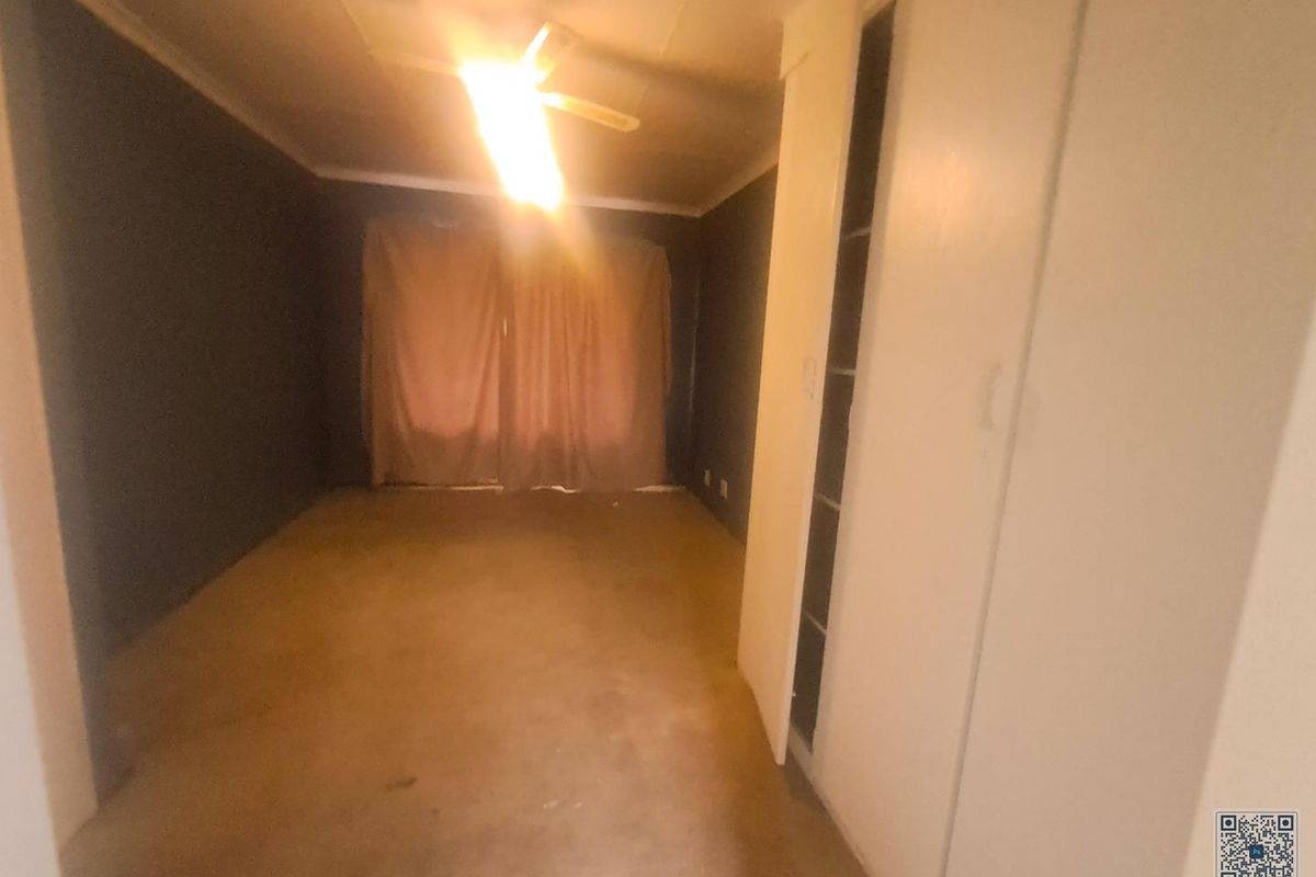 An empty bedroom featuring built-in cupboards and a ceiling fan, requiring cosmetic updates to modernize the space.