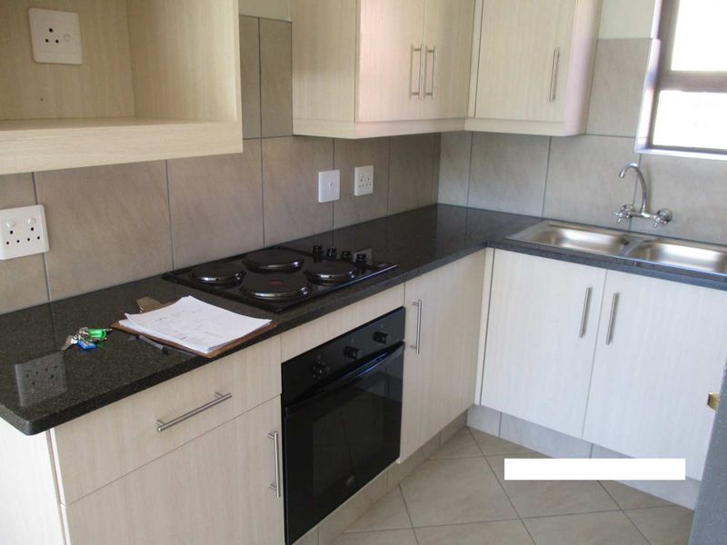 A functional kitchen featuring light wood cabinetry, dark granite countertops, a built-in oven, electric hob, and a stainless steel sink with tiled backsplash.