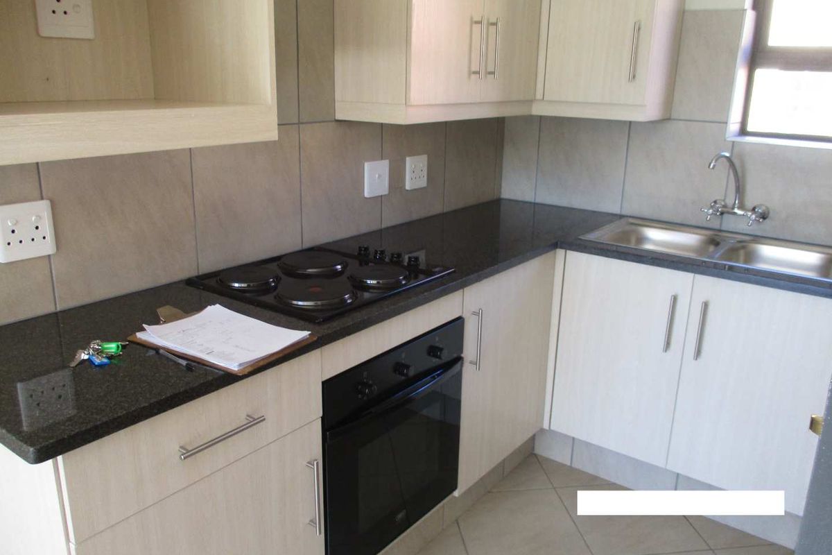 A functional kitchen featuring light wood cabinetry, dark granite countertops, a built-in oven, electric hob, and a stainless steel sink with tiled backsplash.