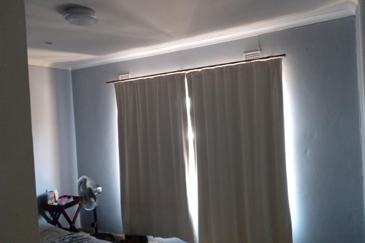 A bedroom featuring neutral grey walls, recessed ceiling lighting, and a window fitted with a curtain rod.