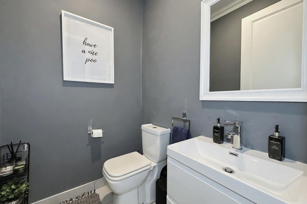 A modern guest cloakroom featuring a sleek vanity basin with chrome mixer tap, a white toilet, and a framed wall mirror.