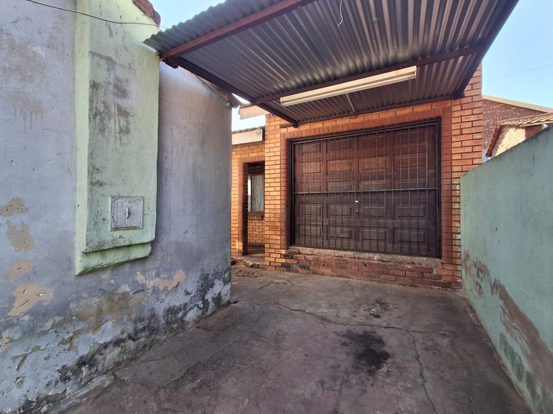 A detached brick garage featuring a corrugated metal roof, security gate, and concrete driveway, showing significant signs of wear and exterior maintenance requirements.