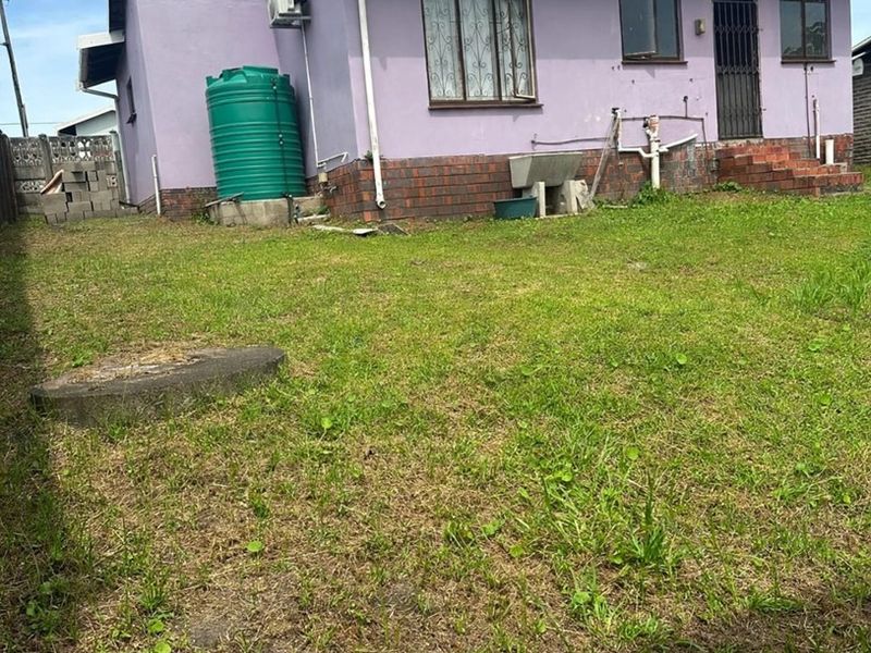 Rear view of the property featuring a lawn, exterior water tank, air conditioning unit, and brick foundation detailing.