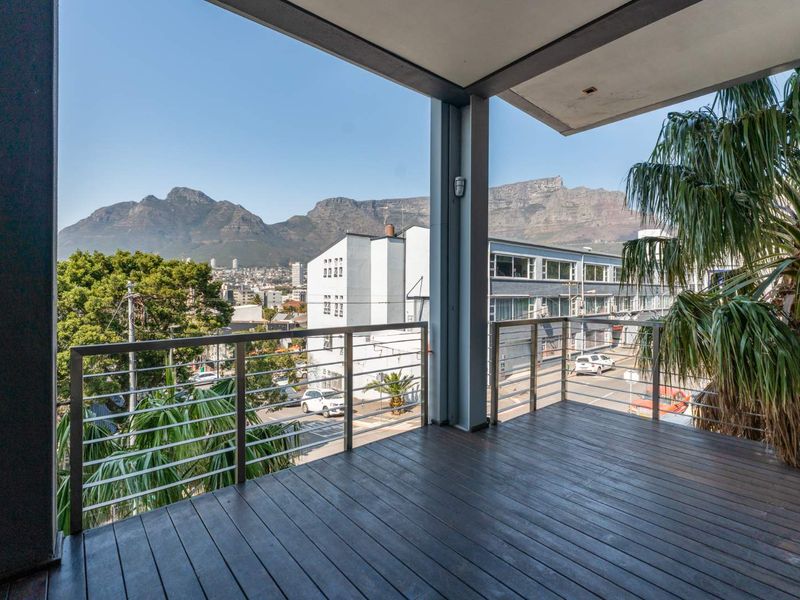 Spacious covered balcony featuring timber decking and a metal balustrade, offering expansive mountain and urban views.