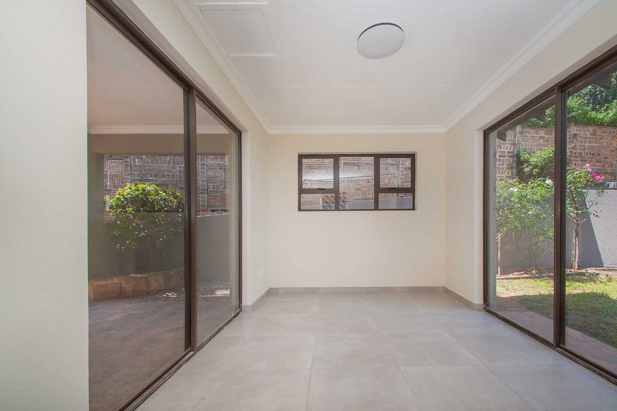 A bright, empty living area featuring large sliding glass doors that provide ample natural light and direct access to the outdoor garden space.