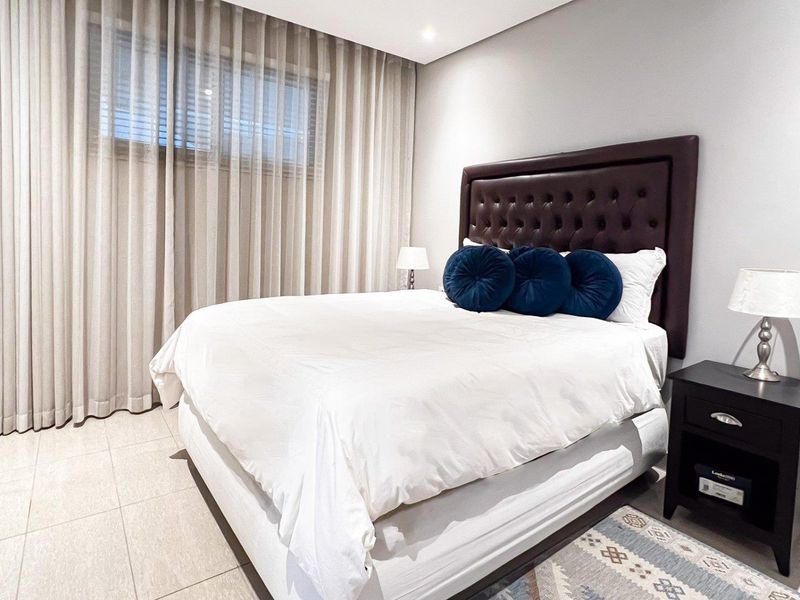 A well-maintained bedroom featuring tiled flooring, recessed ceiling lighting, built-in wardrobes, and floor-to-ceiling window curtains.