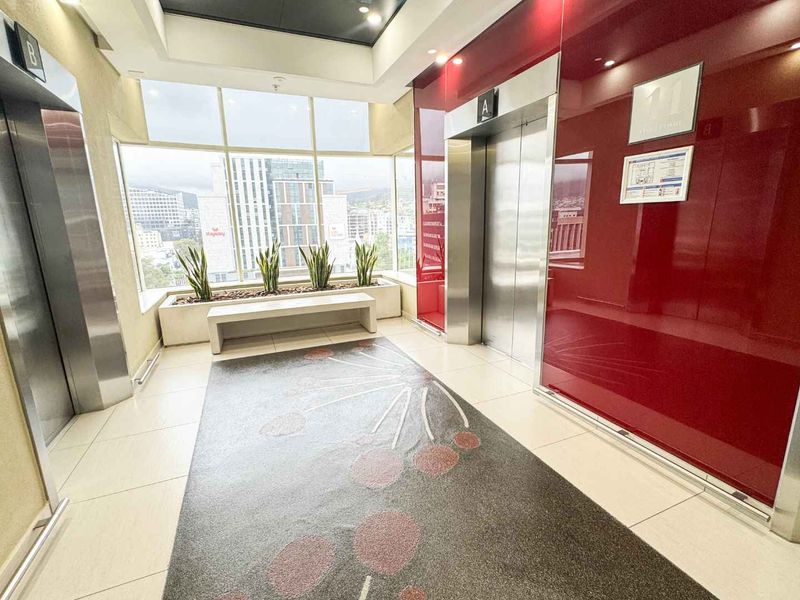 Modern office building elevator lobby featuring stainless steel elevator doors, large windows with city views, and a built-in planter box.
