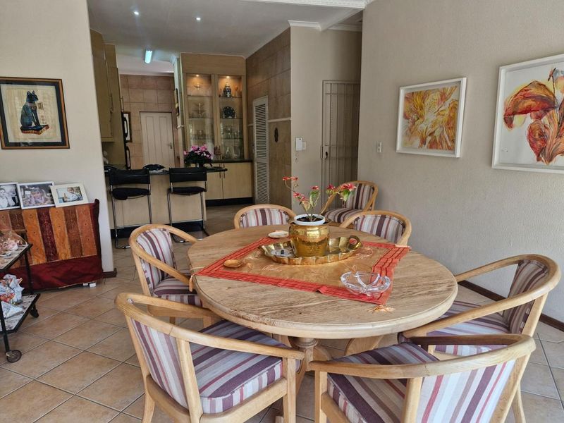 Open-plan dining area featuring tiled flooring and recessed lighting, flowing into a kitchen space with built-in display cabinetry and a breakfast bar.