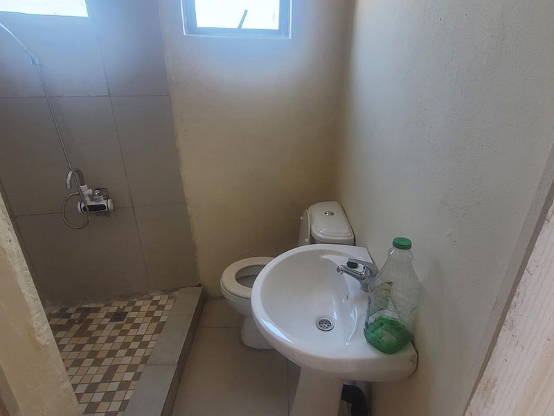A compact bathroom featuring a pedestal sink, toilet, and a tiled shower area with a wall-mounted mixer.