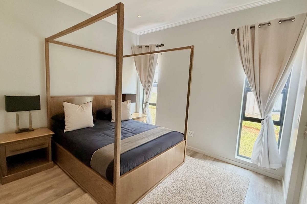 A well-maintained bedroom featuring light wood-look flooring, neutral wall tones, and large windows that provide natural light.