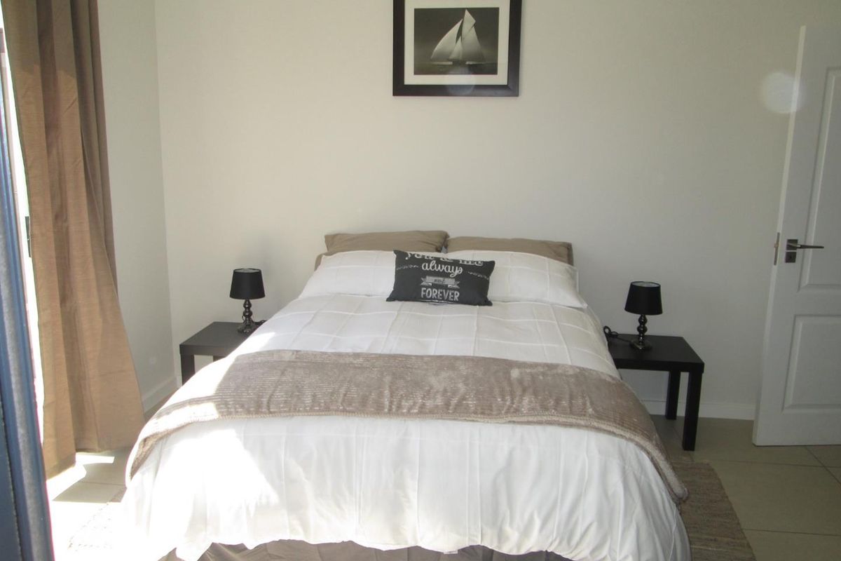 A well-maintained bedroom featuring neutral wall tones, tiled flooring, and direct access to an outdoor area via a sliding door.