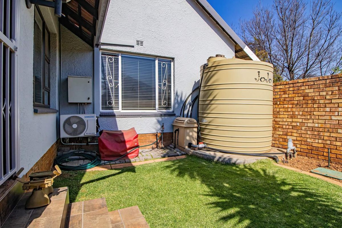 Rear exterior area featuring a water storage tank, brick boundary wall, and air conditioning unit, with tiled steps leading to the garden space.