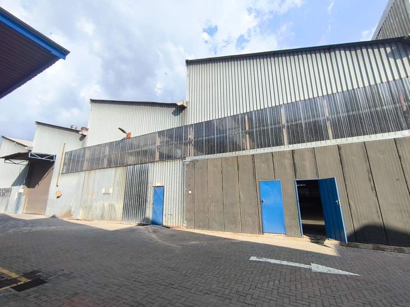 Exterior view of an industrial warehouse facility featuring corrugated metal cladding, translucent wall panels, and paved access area with multiple steel entry doors.