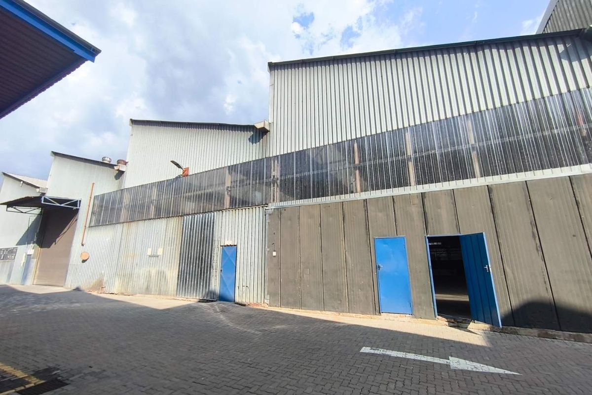 Exterior view of an industrial warehouse facility featuring corrugated metal cladding, translucent wall panels, and paved access area with multiple steel entry doors.