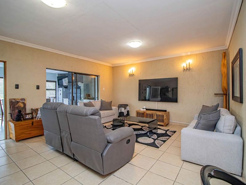 A spacious living room featuring neutral tiled flooring, textured wall finishes, and direct access to an adjacent area through a sliding glass door.