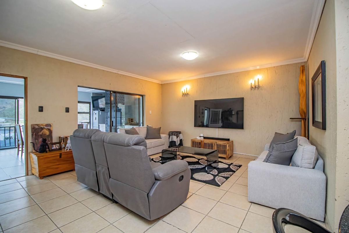 A spacious living room featuring neutral tiled flooring, textured wall finishes, and direct access to an adjacent area through a sliding glass door.