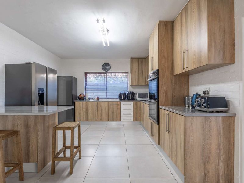 Modern kitchen featuring wood-finish cabinetry, stone countertops, a breakfast bar, and tiled flooring, offering a clean and functional workspace.