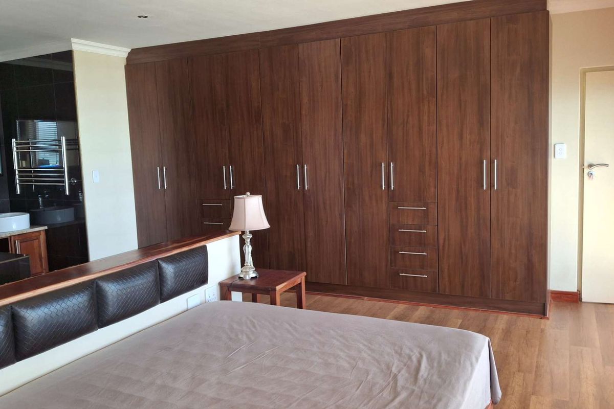 Spacious bedroom featuring extensive dark wood built-in cupboards, laminate flooring, and direct access to an en-suite bathroom.