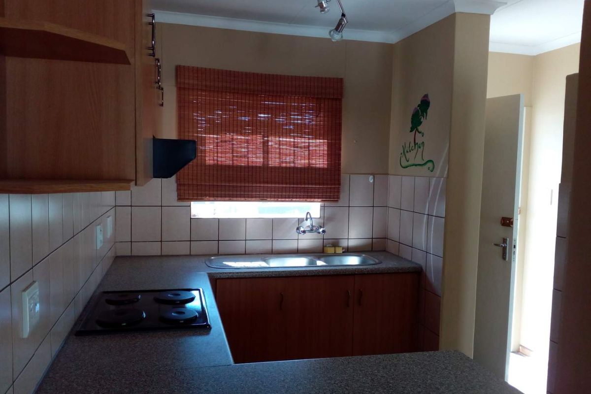 Functional kitchen featuring laminate cabinetry, double bowl stainless steel sink, electric hob, extractor fan, and tiled backsplash.