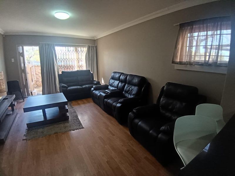 A spacious living room featuring laminate flooring, a sliding door with security gate, and neutral wall finishes, offering a comfortable and functional living space.