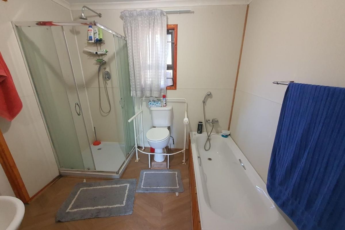 A functional bathroom featuring a glass-enclosed shower, a standard bathtub with handheld shower attachment, and a toilet with safety rails.