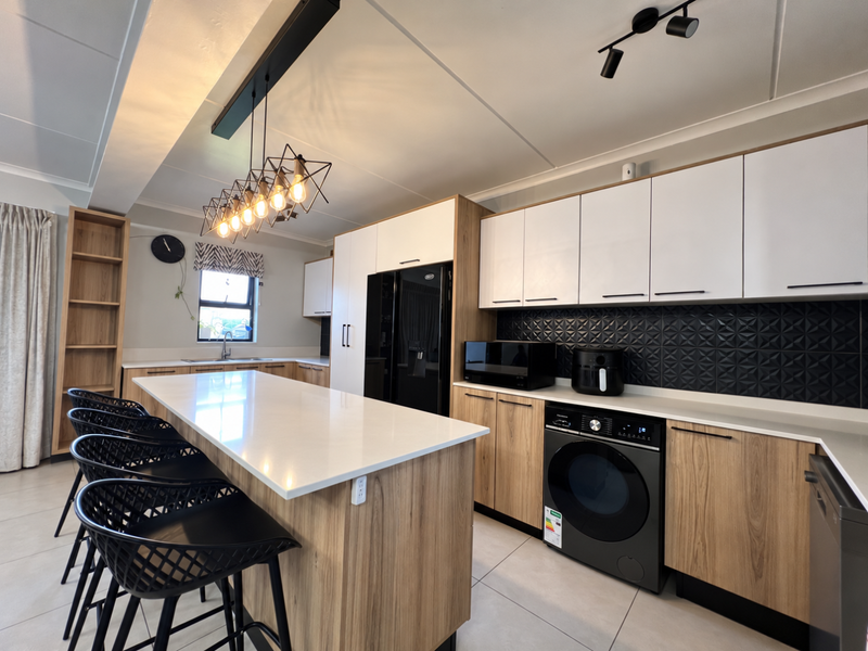 Modern kitchen featuring a large island with quartz countertops, sleek two-tone cabinetry, textured backsplash, and integrated appliances in a well-lit, contemporary space.