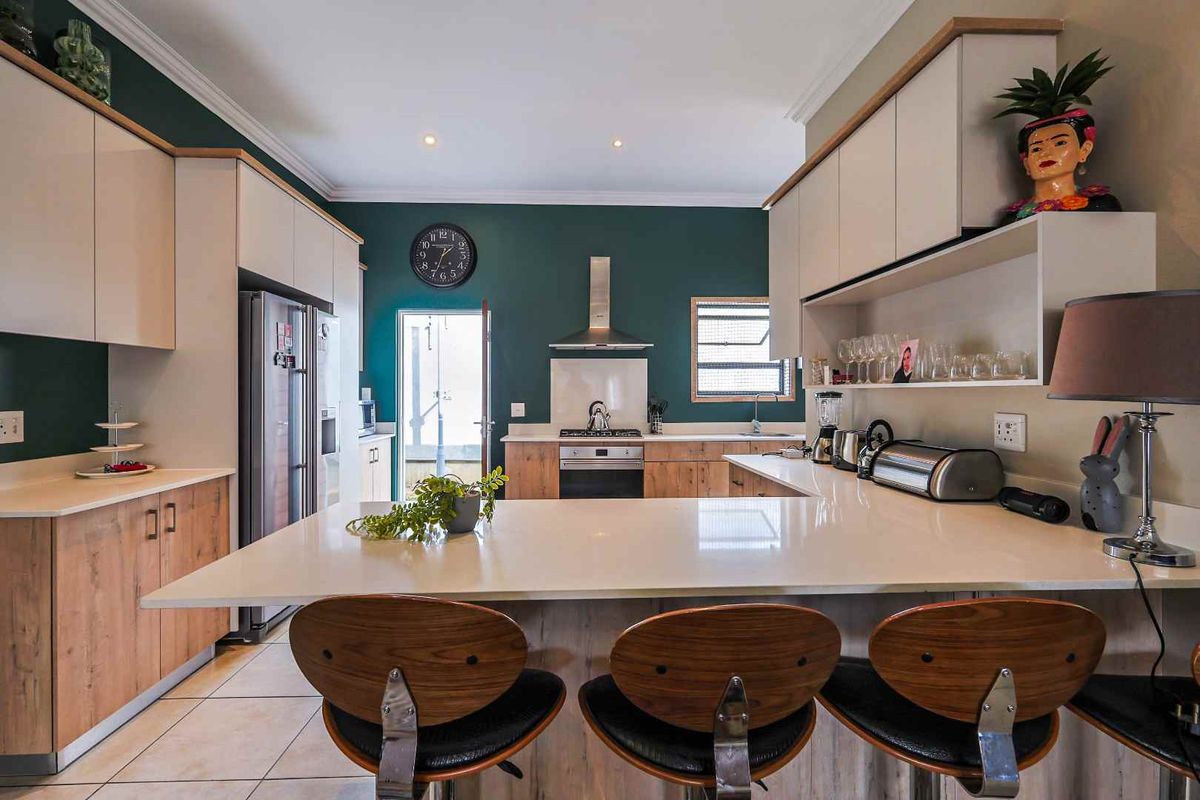 Modern kitchen featuring two-tone cabinetry, stone countertops, a breakfast bar, and integrated stainless steel appliances with a stylish dark accent wall.