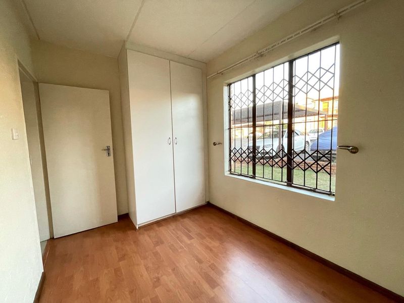 A vacant bedroom featuring laminate flooring, a built-in wardrobe, and a window fitted with a security gate.