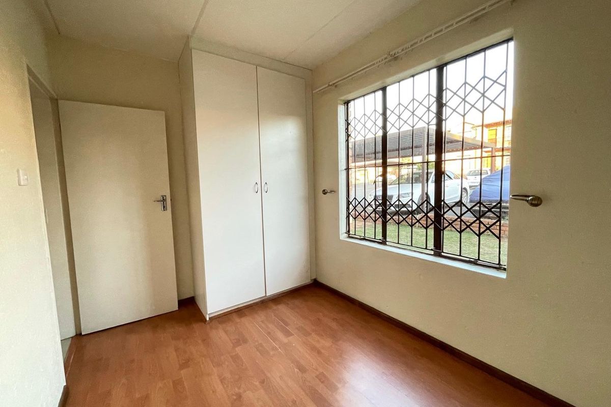 A vacant bedroom featuring laminate flooring, a built-in wardrobe, and a window fitted with a security gate.