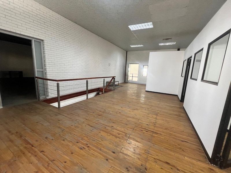 An open-plan office space featuring timber flooring, exposed brick walls, and recessed ceiling lighting, offering a versatile layout for business operations.