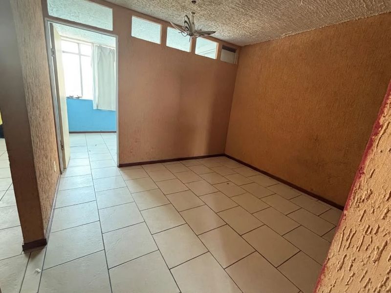 An empty living area featuring ceramic floor tiles, textured walls, and transom windows, offering a blank canvas for renovation and interior design.