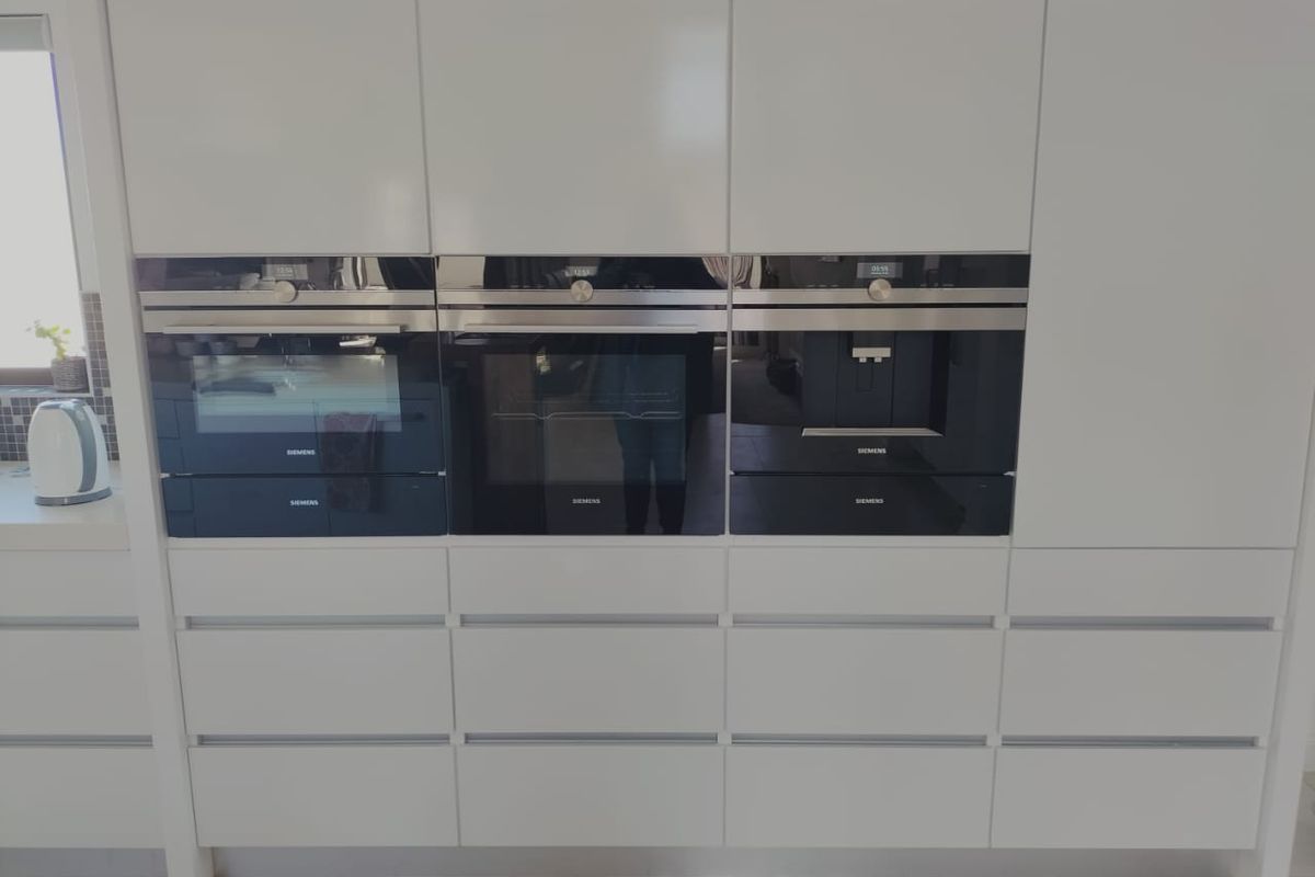 Modern kitchen featuring a bank of high-end integrated Siemens appliances, including ovens and a coffee machine, set within sleek white cabinetry.