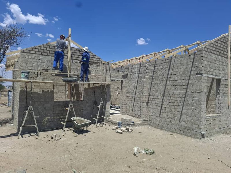 A residential property currently under construction, featuring exposed concrete block walls and timber roof trusses in the early stages of development.