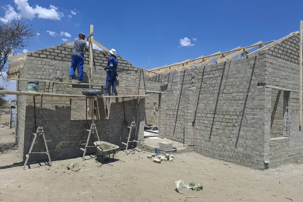 A residential property currently under construction, featuring exposed concrete block walls and timber roof trusses in the early stages of development.