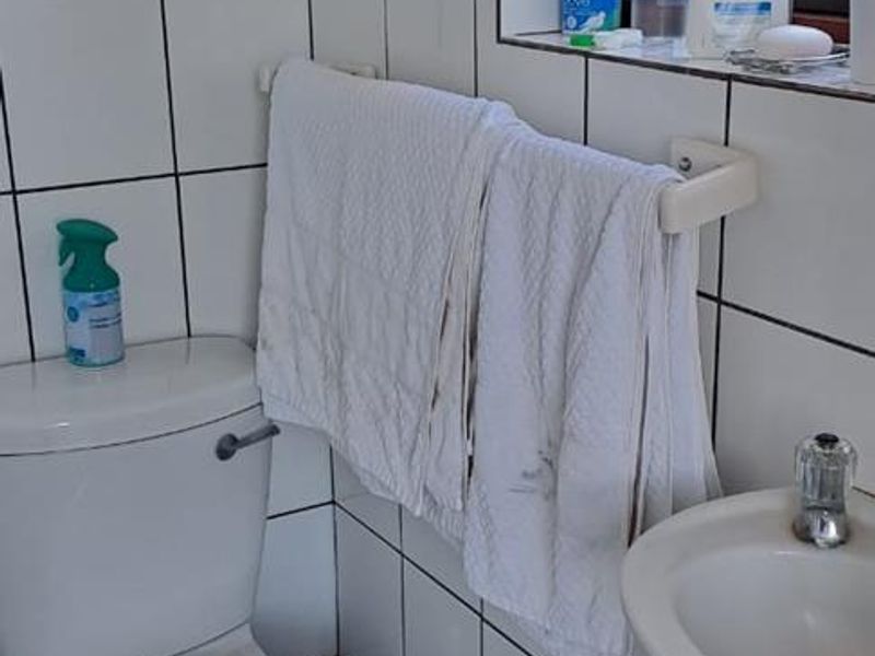 A compact bathroom featuring white wall tiles, a standard toilet, and a pedestal basin, requiring some maintenance and cosmetic updates.