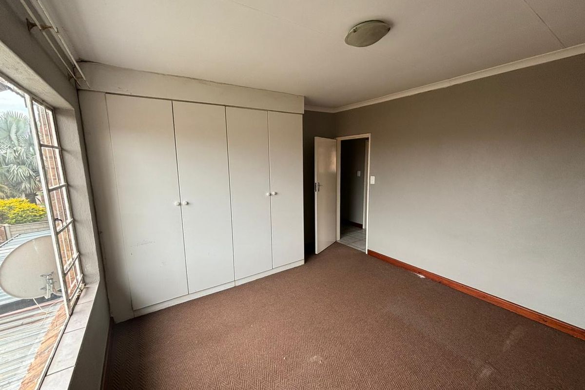 A bedroom featuring built-in wardrobes, carpeted flooring, and a large window providing natural light.