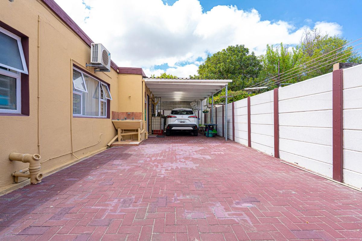 A paved driveway leading to a covered carport area, featuring a concrete boundary wall and exterior utility sink.