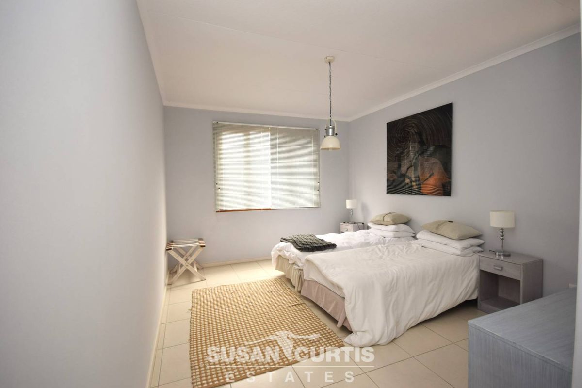 A well-lit bedroom featuring neutral tiled flooring, a pendant light fixture, and a window with fitted blinds.
