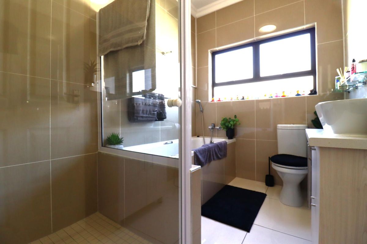 A functional bathroom featuring a glass-enclosed shower, a built-in bathtub, a toilet, and a vanity basin with tiled walls and flooring.