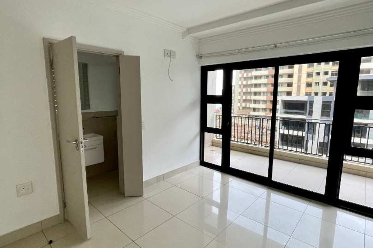 A bright, empty bedroom featuring large sliding glass doors leading to a balcony, tiled flooring, and a built-in closet area.