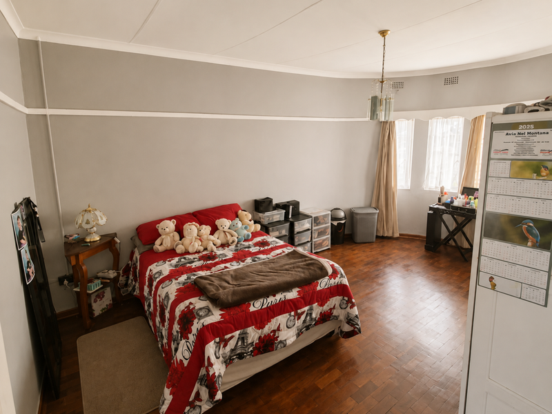 A spacious bedroom featuring warm parquet flooring, coved ceilings, and a central light fixture, offering a comfortable and well-maintained living space.