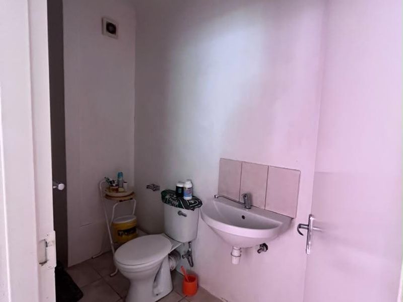 A compact bathroom featuring a wall-mounted basin, toilet, and tiled flooring, currently requiring cosmetic updates and finishing touches.