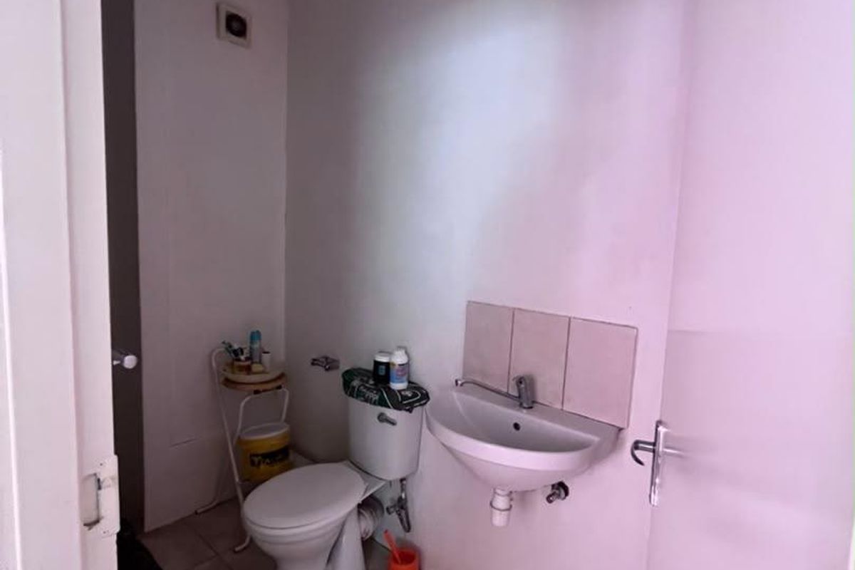 A compact bathroom featuring a wall-mounted basin, toilet, and tiled flooring, currently requiring cosmetic updates and finishing touches.