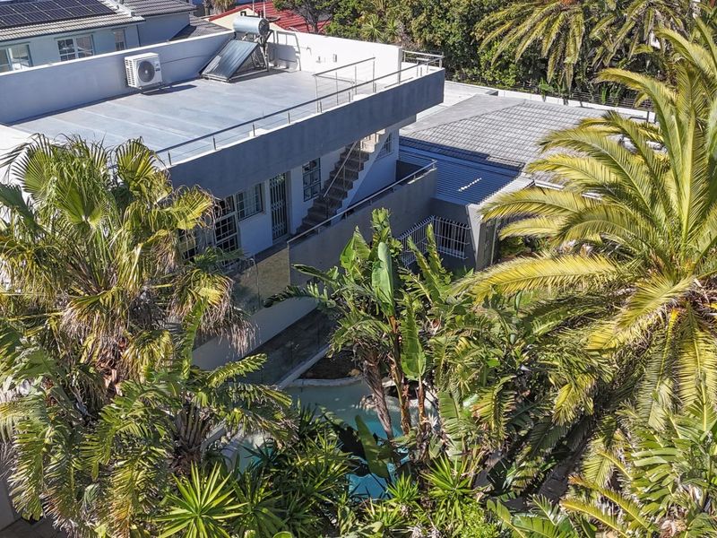 Aerial view of the property featuring a flat roof with solar water heating, an external staircase, and a swimming pool surrounded by lush landscaping.