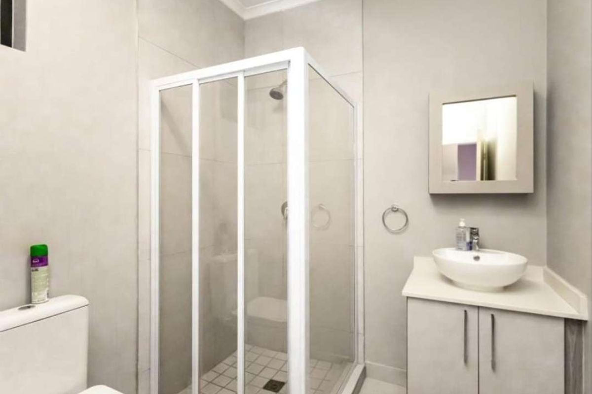 A clean, modern bathroom featuring a glass shower enclosure, a vessel sink vanity, and neutral wall tiling.