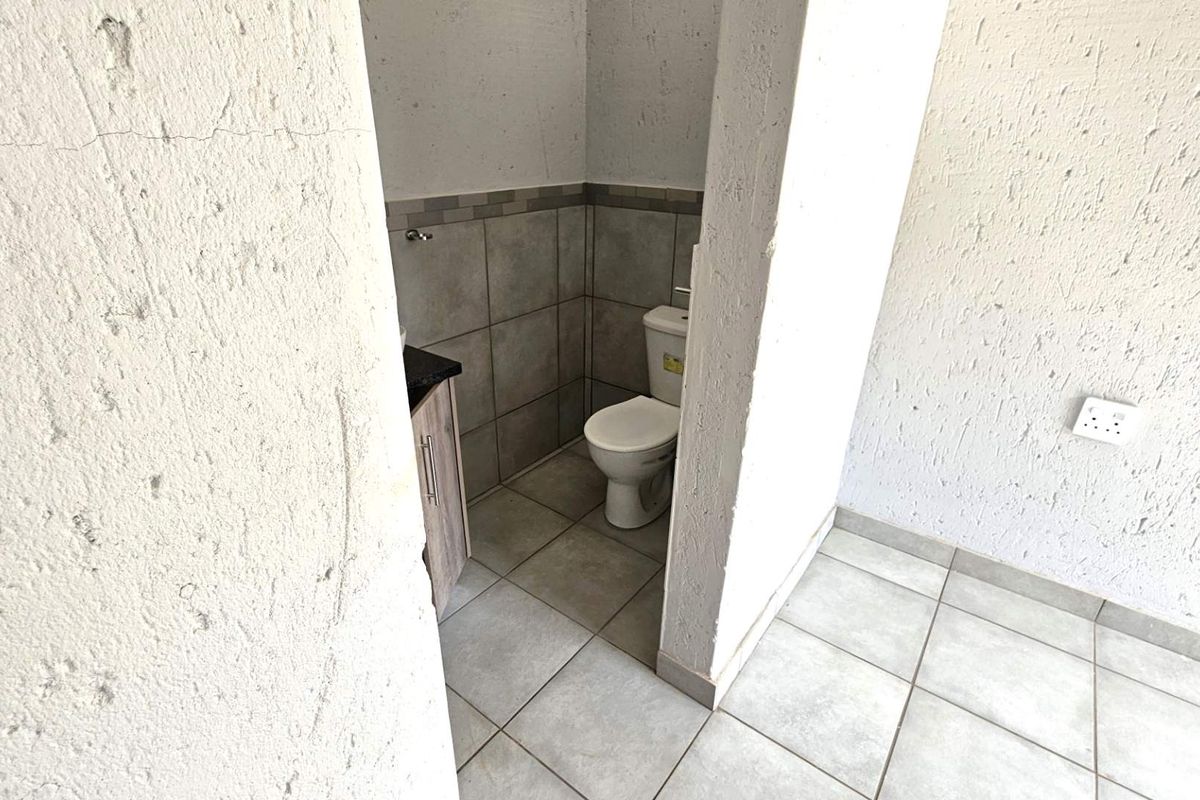A compact bathroom featuring tiled flooring, a built-in vanity cabinet, and a standard toilet, requiring cosmetic attention to wall finishes.