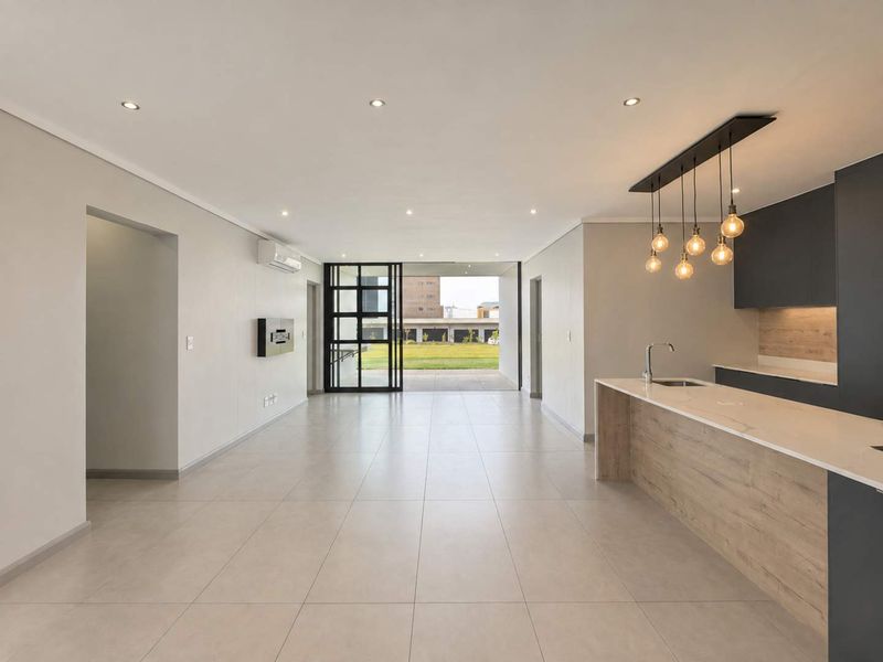 Modern open-plan living and kitchen area featuring sleek cabinetry, stone countertops, tiled flooring, and large sliding doors leading to an outdoor space.