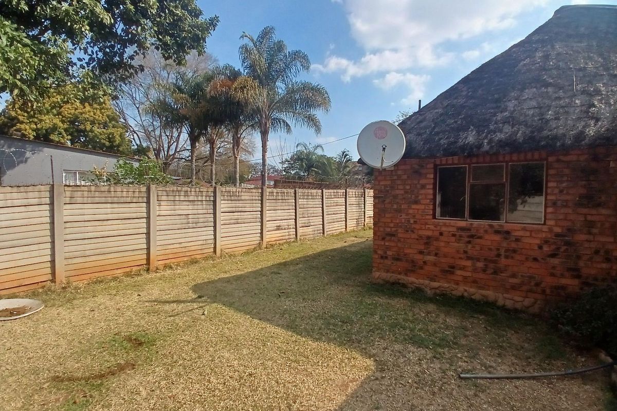 Rear exterior view of the property featuring a brick building with a thatch roof, a large lawn, and a precast concrete boundary wall.
