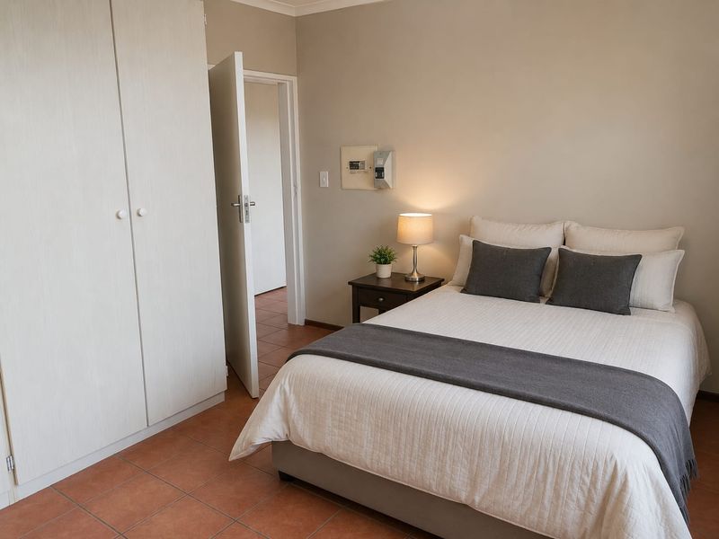A well-maintained bedroom featuring built-in wardrobes, neutral wall tones, and durable tiled flooring.